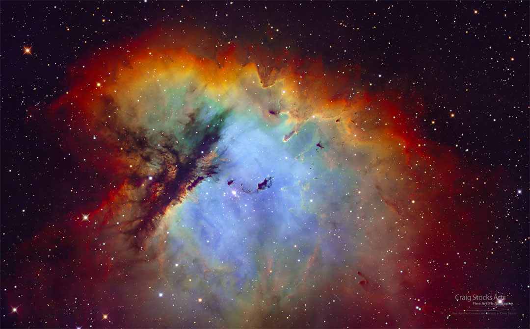 A nebula that appears blue in the middle and is surrounded by
red-glowing gas is featured. Dramatic lanes of dark dust cut
through the nebula's left side. A group of stars is visible toward
the nebula's center.
Please see the explanation for more detailed information.