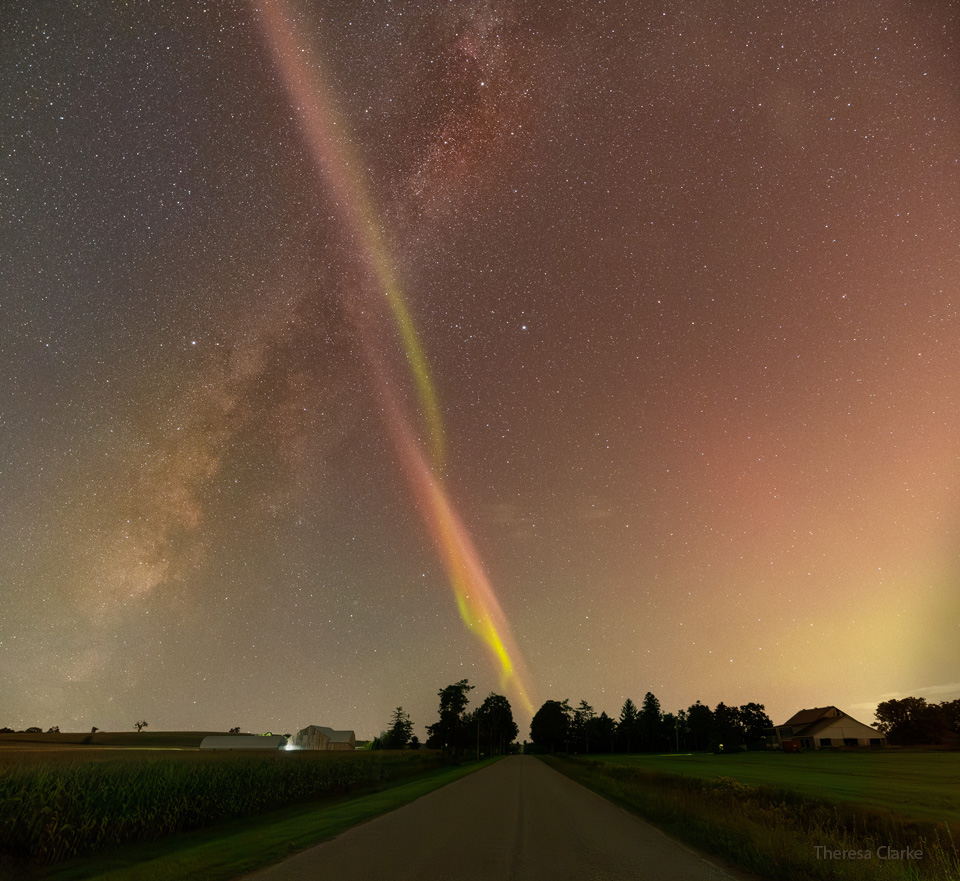 A rural road is pictured running to the horizon with rural
grassy fields on both sides. Rising from the lower left is the
central band of our Milky Way Galaxy. Rising from the horizon
-- just at the visible end of the road, is a thin twisting band
of light twisting green and red bands -- a STEVE. The STEVE
crosses in front of the Milky Way band making a big 