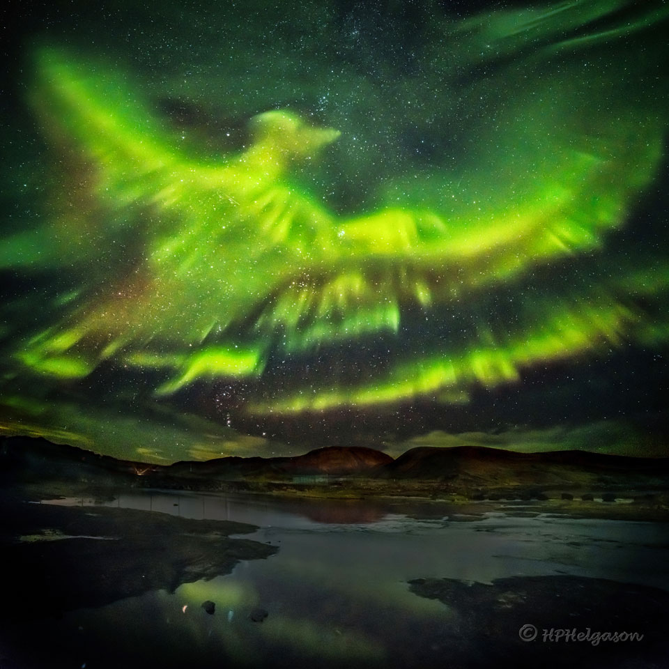 A green aurora fills a star filled sky. A mountain and a lake
are in the foreground. The aurora may resemble, to some, a flying
or rising Phoenix. 
Please see the explanation for more detailed information.